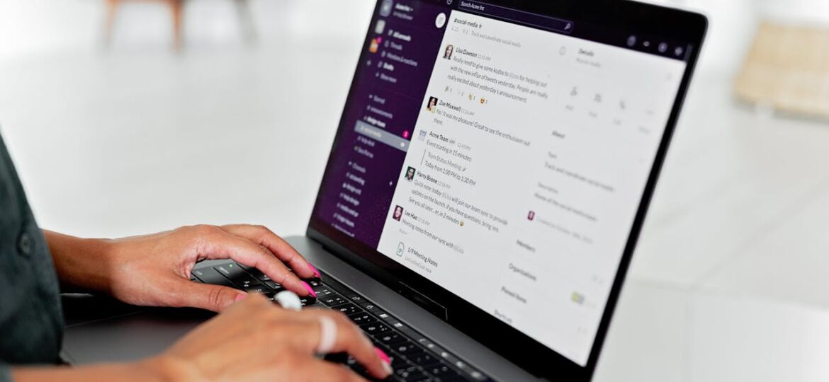 A woman types on a laptop using a messaging app in a modern office setting.