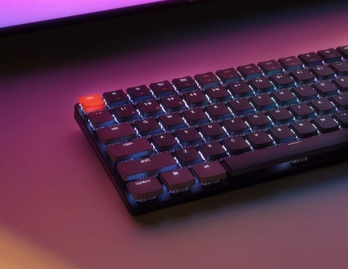 Illuminated desk setup with keyboard and monitor in vibrant pink lighting.