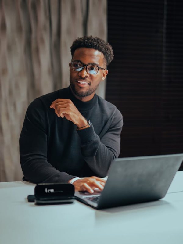 Cheerful man with glasses working on laptop at a table indoors, emanating a professional and modern workspace vibe.