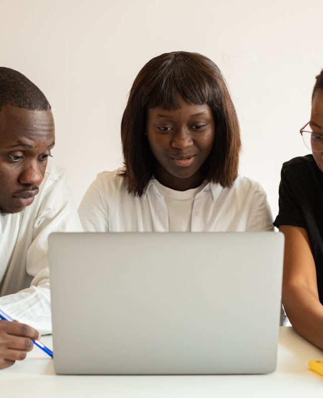 Three professionals working together on a project using a laptop in an office setting.